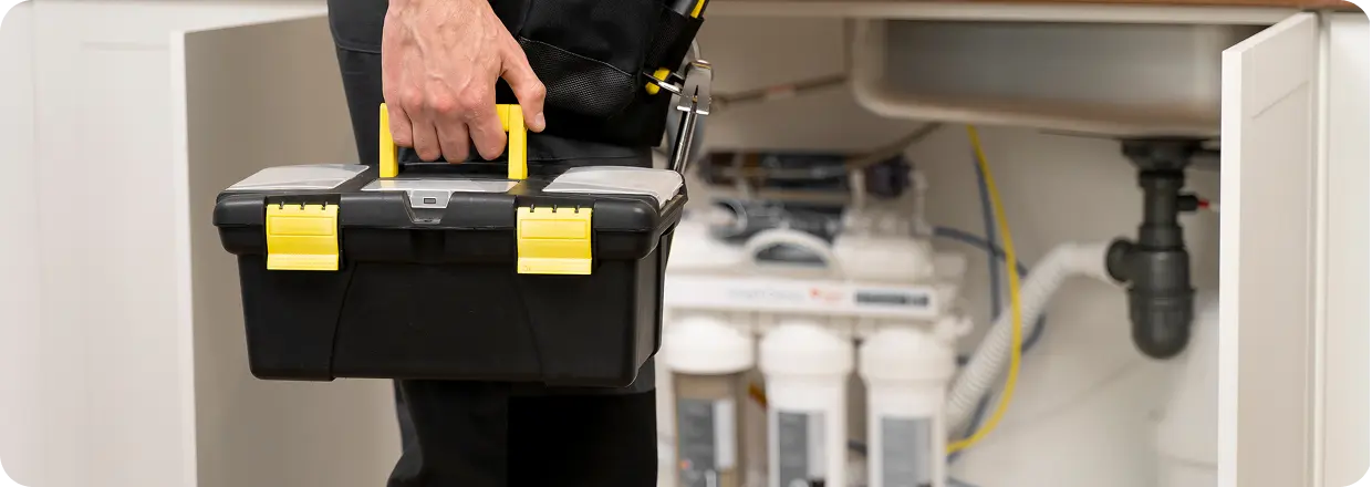 technicus met een gereedschapskist bij het onderliggende loodgietersysteem, die woningreparatie, onderhoud van watersystemen en professionele loodgietersdiensten vertegenwoordigt